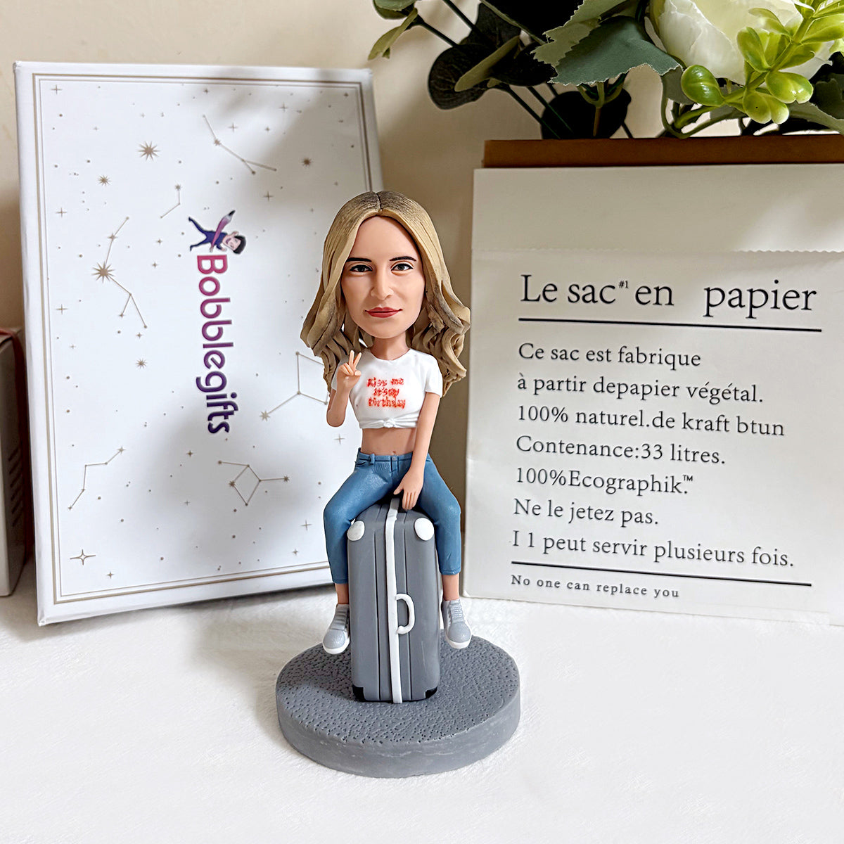 Figurine à tête branlante personnalisée posée sur une valise