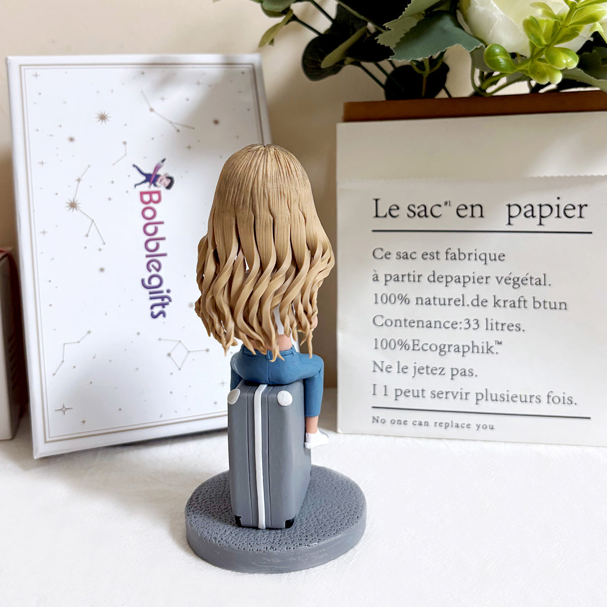 Figurine à tête branlante personnalisée posée sur une valise